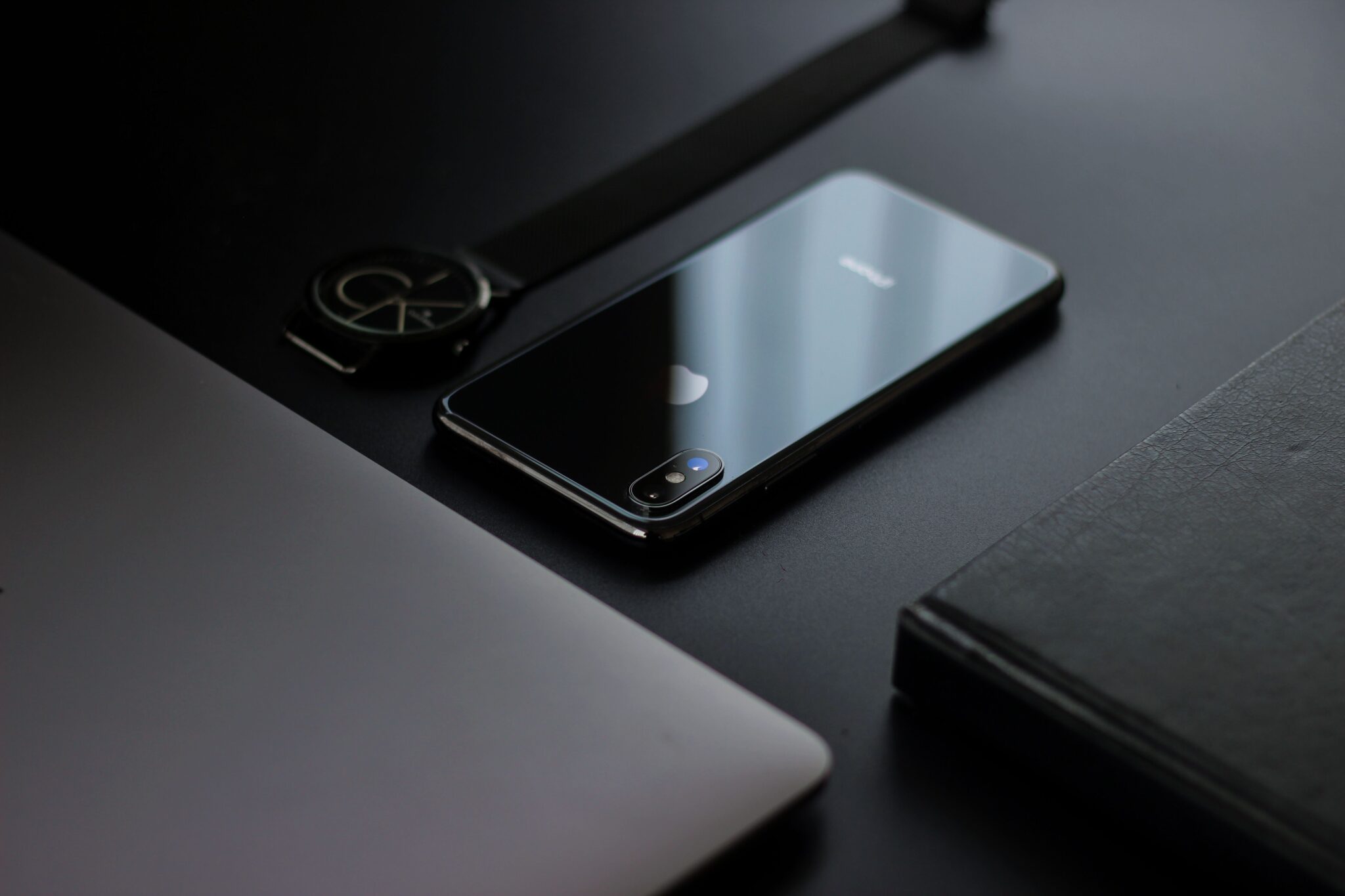Sleek workspace featuring a smartphone, wristwatch, and laptop on a dark surface.